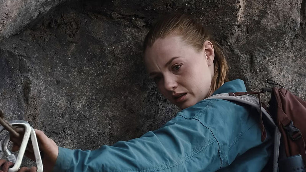 Female rock climber in a blue jacket grips a carabiner on a rugged cliff, looking tense and focused with a backpack on her shoulder.