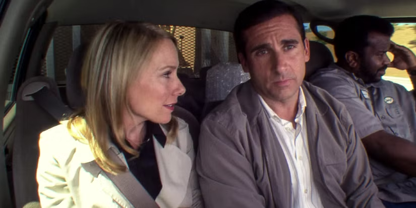 Three adults ride in a car; a blonde woman talks to a serious man while the driver looks ahead.