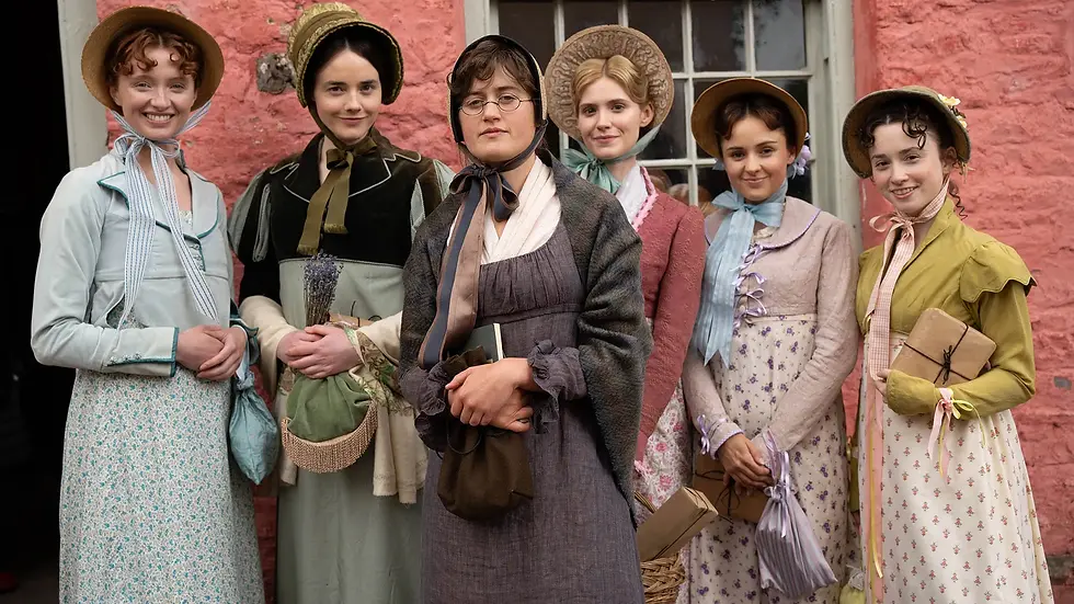 Six women in bonnets and long dresses stand smiling outside a pink cottage, holding books and parcels.