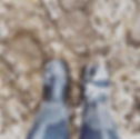 Boots stand in slushy, muddy ground with patches of snow. The scene shows a messy, wintry outdoor setting with wet, black boots.