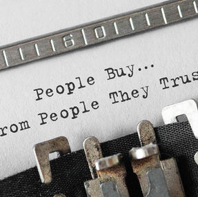 Close-up of a typewriter typing the text "People Buy... From People They Trust" on white paper. The image conveys trust in transactions.