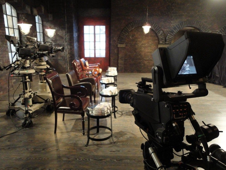 Studio ze zákulisí s kamerovou technikou a čtyřmi židlemi.