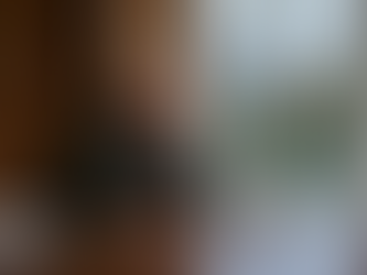 A professional photograph of a thoughtful senior leader, seated alone at a desk looking out over the grounds of an independent school. 