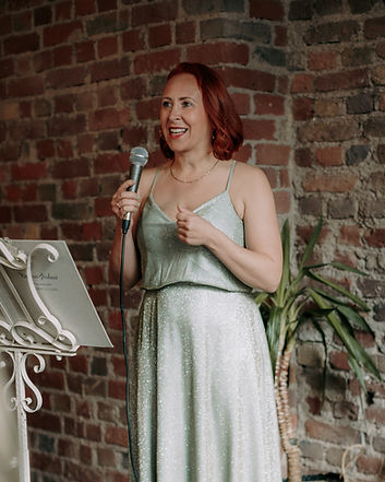 Magdalena, freie Rednerin in einem schönen grünen Kleid und Mikrofon in der Hand beim Sprechen.