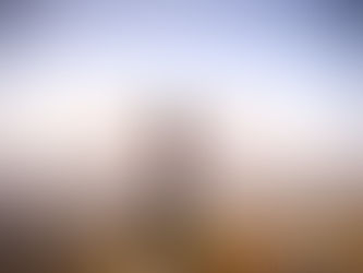 Lady on a cliff with arms outstretched, facing a hazy valley under a bright blue sky, conveying freedom and awe.