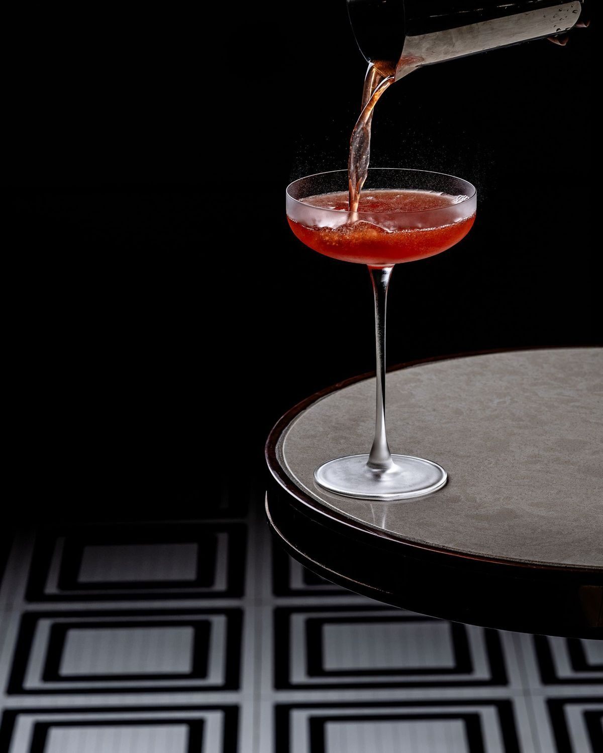 Red cocktail being poured into a coupe