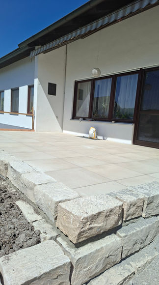 Moderne Terrasse mit großformatigen Terrassenplatten und Naturstein-Stufen an einem Einfamilienhaus in Schwäbisch Hall.