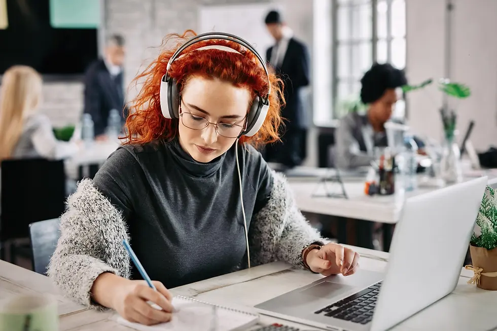 redhead-businesswoman-using-laptop-writing-notes-her-notepad-while-listening-music-headpho