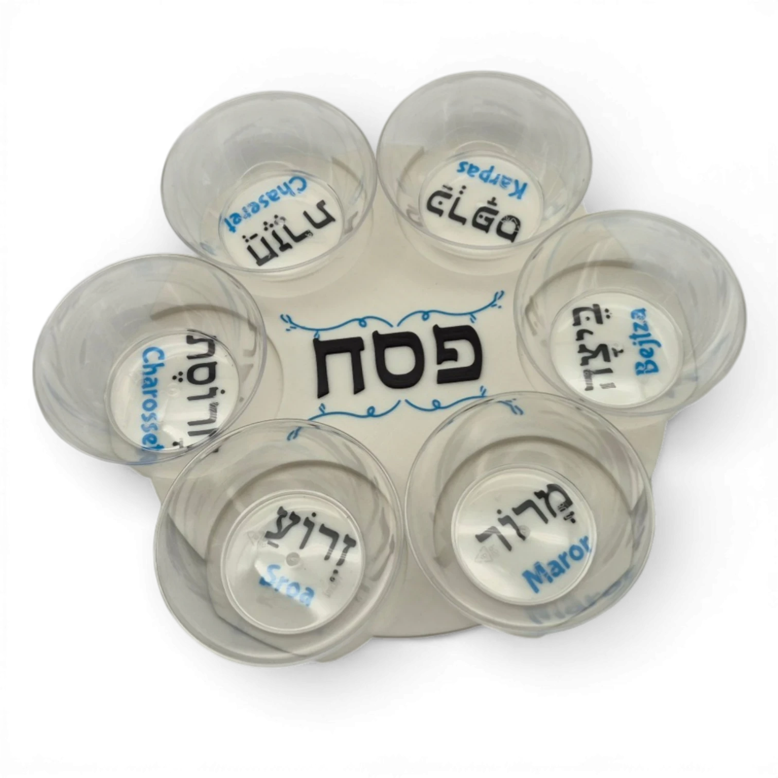 Seder-Set mit sechs transparenten Kunststoffschälchen auf einer runden Platte vor schwarzem Hintergrund