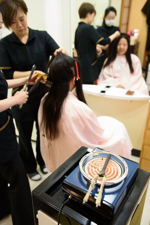 花嫁の地毛を使って日本髪を結い上げる準備。美容師たちが息を合わせ、丁寧に髪を分け取りながら形を作っていく。