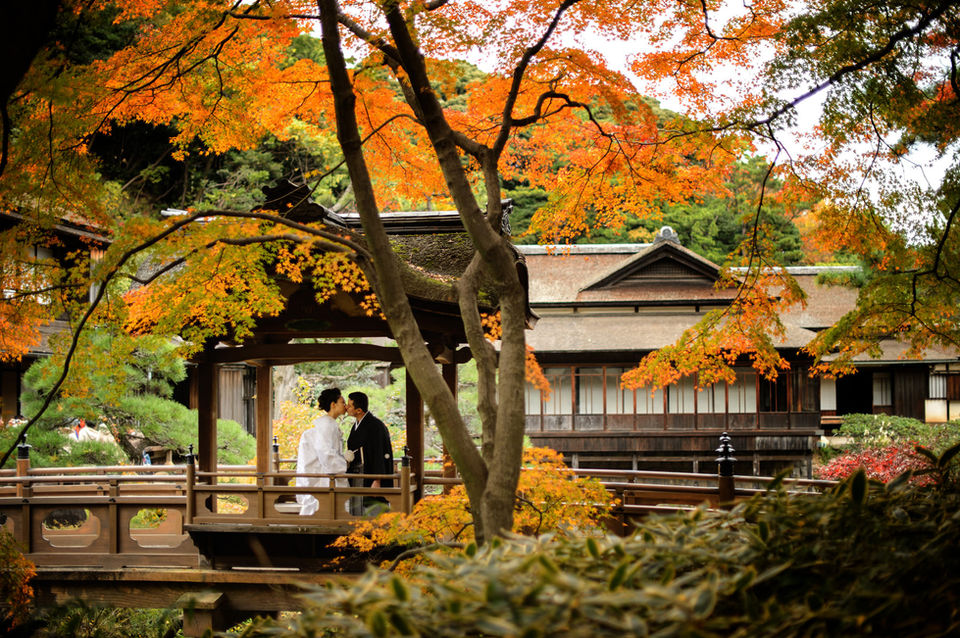 三渓園で紅葉に彩られた庭園の回廊で見つめ合う新郎新婦、秋の和装ロケーション撮影
