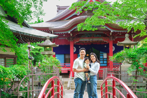 井の頭公園の赤い橋の上で、弁財天を背景に笑顔で立つ家族。新緑に囲まれた吉祥寺の人気撮影スポットでのロケーションフォト。