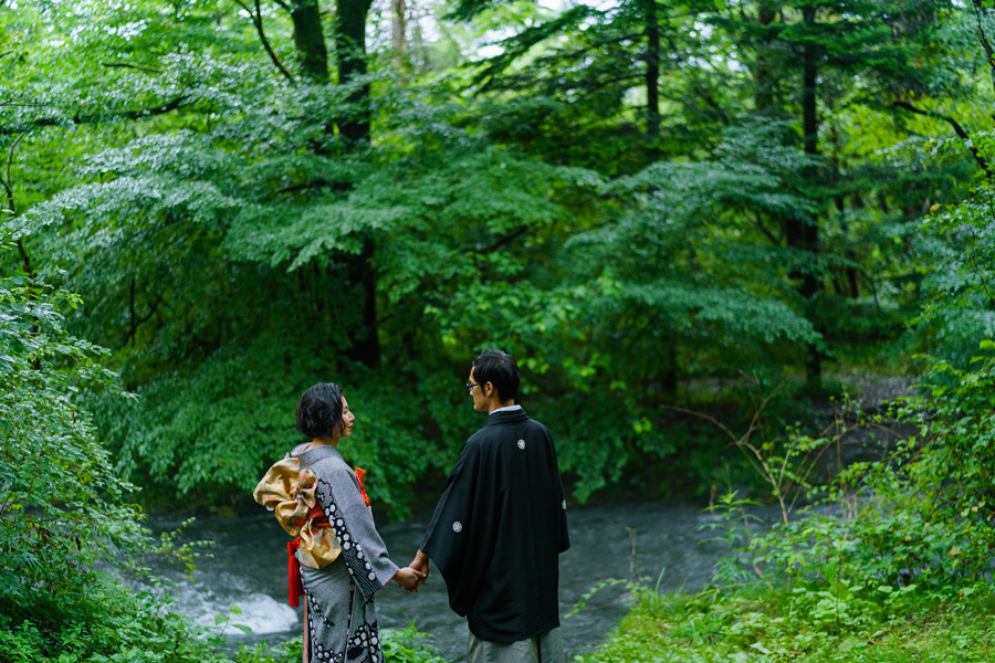 川沿いの森を背景に、手を取り合って立つ和装姿の新郎新婦