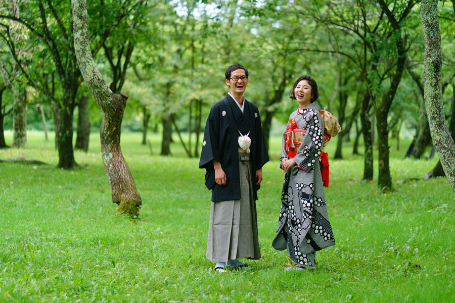 木々に囲まれた草原を歩く和装の新郎新婦、自然あふれる軽井沢にて