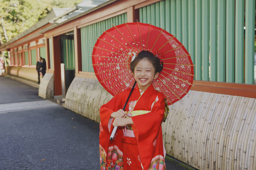 赤い和傘を持って笑顔を見せる7歳の七五三ポートレート｜赤坂日枝神社