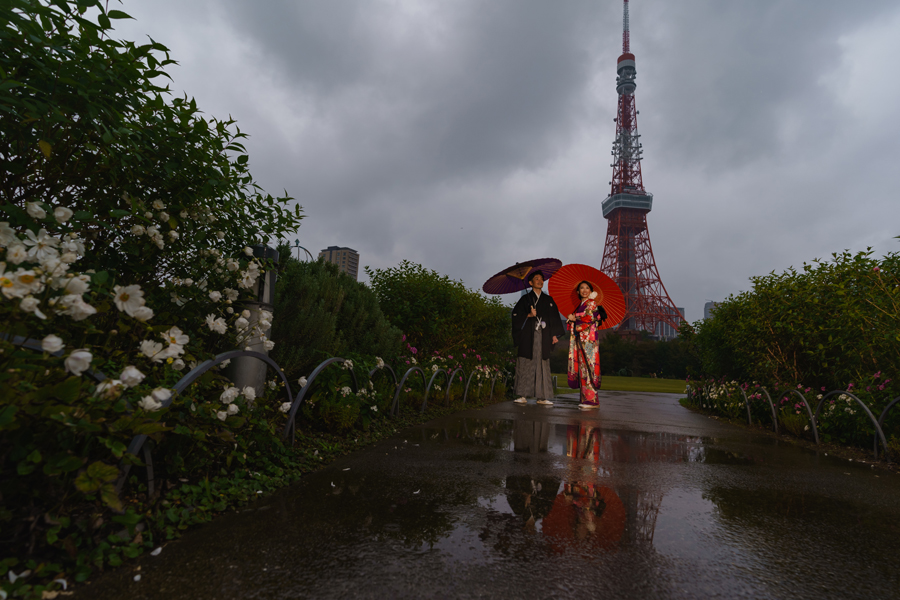 雨上がりの芝公園で、赤と紫の和傘を差した新郎新婦が東京タワー前で立つ姿