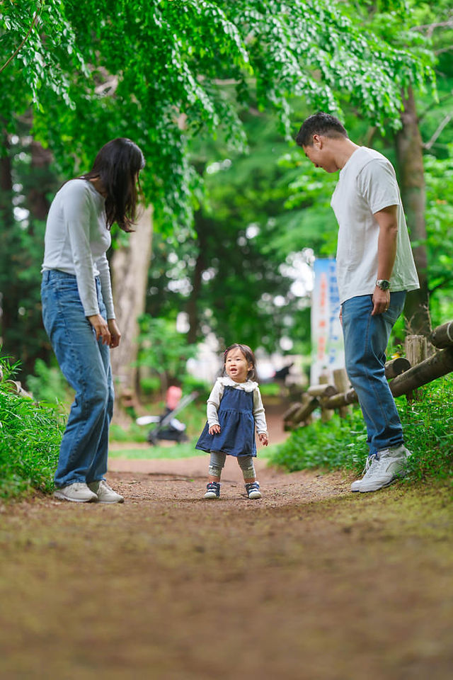 両親に手をつないでもらいながら、井の頭公園を歩く1歳の女の子の記念写真