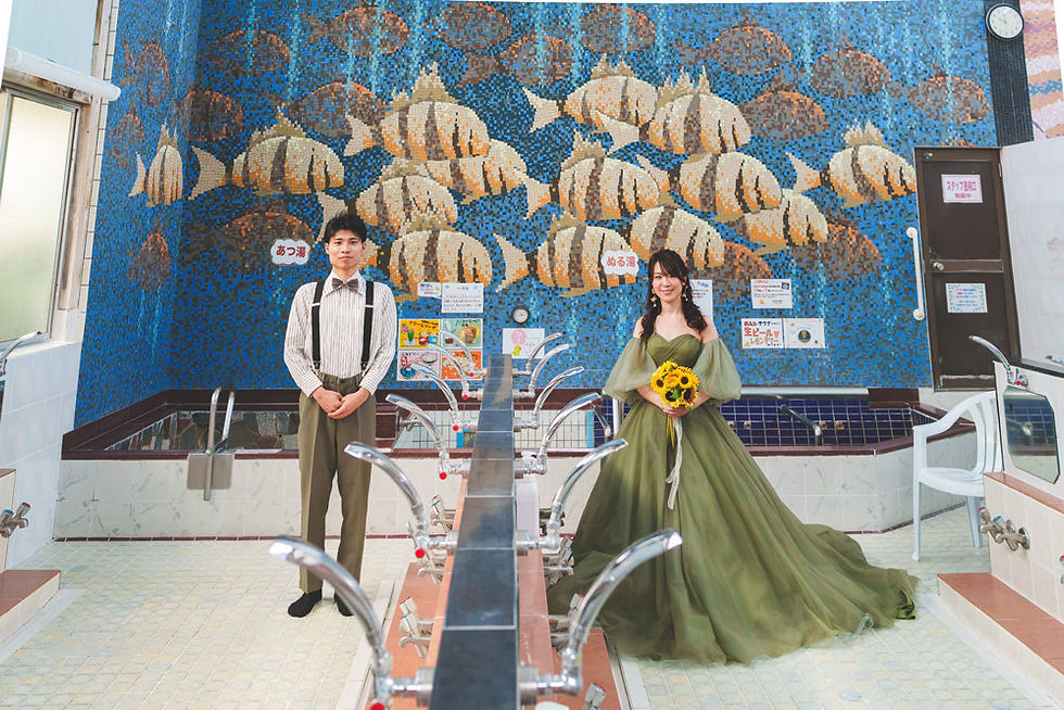 　十條湯男湯の魚群モザイク画を背景に、立ち姿で向日葵を手にする新婦と新郎。