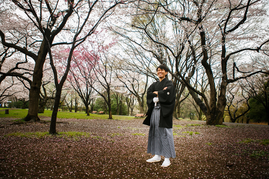 舞い散る桜の花びらの中で立つ新郎、紋付き袴姿で春らしいソロショット