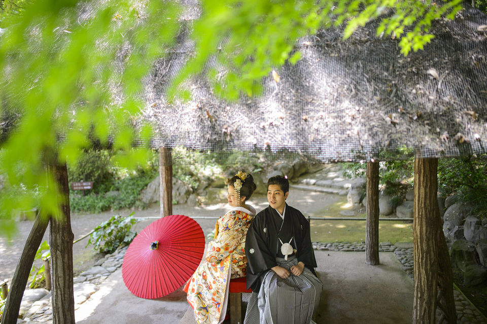 朱色の和傘を横に置き、東屋で寄り添う新郎新婦、色打掛と紋付袴の和装前撮り