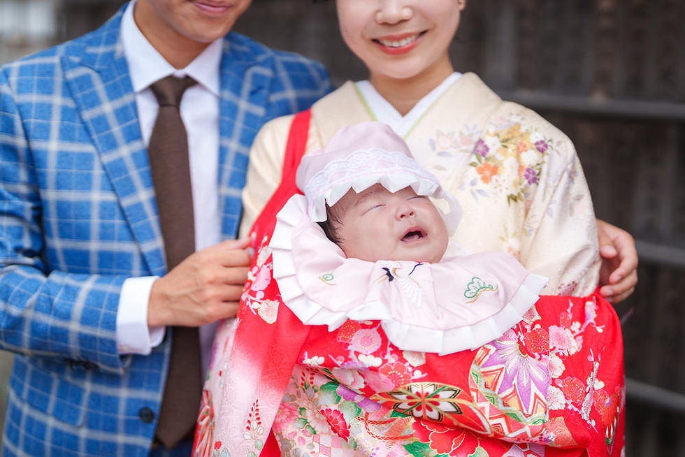 赤い祝い着を着た赤ちゃんを抱く両親のポートレート。母のやさしい笑顔と赤ちゃんの表情が印象的。