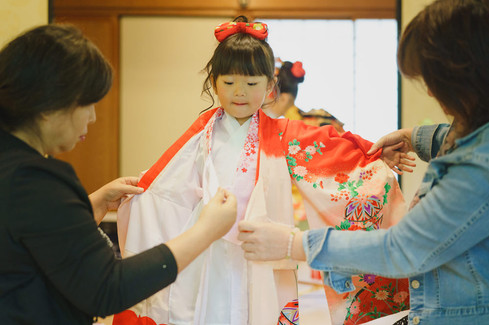 七五三の着物を家族に手伝ってもらいながら着付けをする女の子