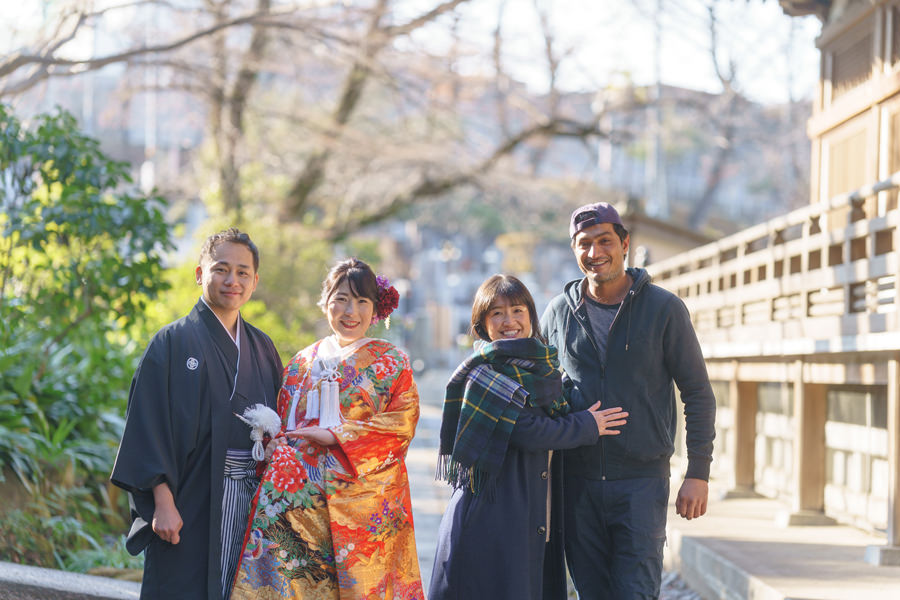 高幡不動尊の参道で、色打掛姿の新婦とお母さまが手を取り合い笑顔で歩く様子