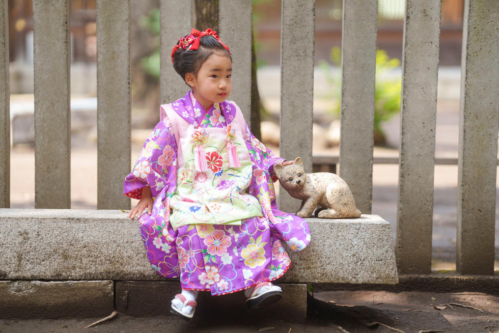 荻窪八幡宮の境内で猫の置物と並んで座る3歳の女の子
