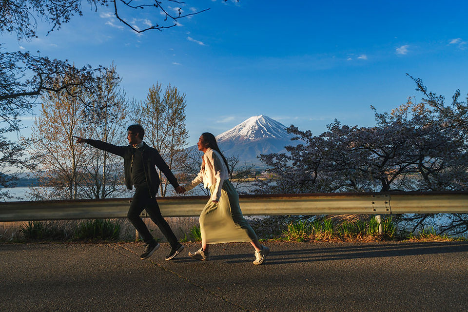 Newly engaged couple walking beneath cherry blossoms with Mt. Fuji in the background during spring in Japan