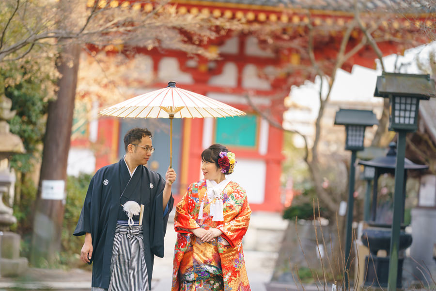 高幡不動尊の境内で、和傘を差して語らう新郎と色打掛姿の新婦