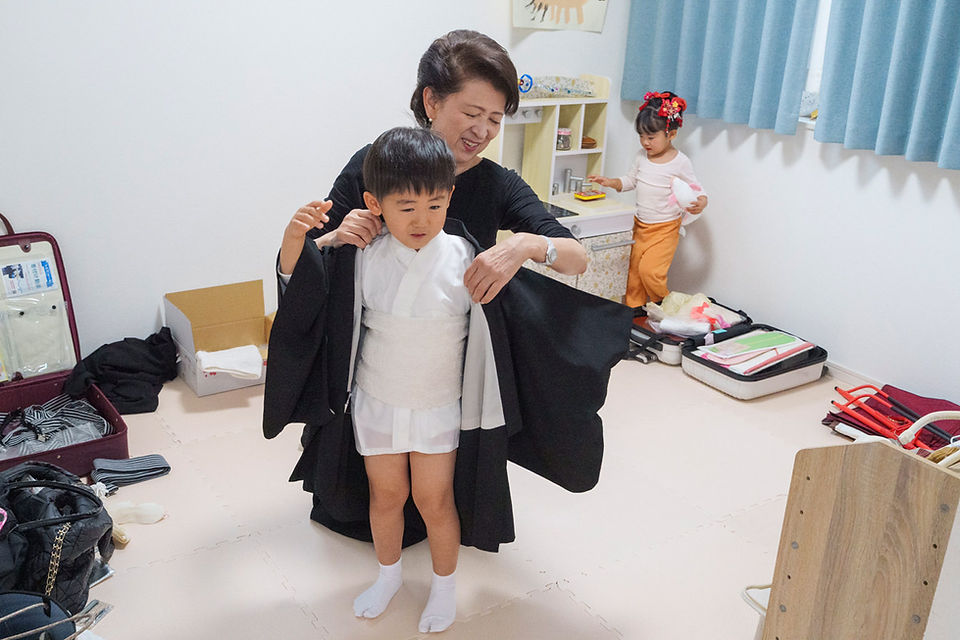 着付け師に七五三の羽織を着せてもらう5歳の男の子