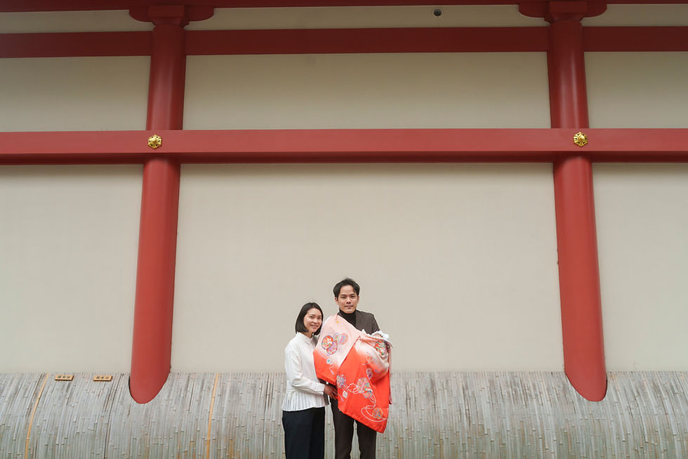 祈祷殿の朱色の壁を背景に撮影したお宮参りの家族写真