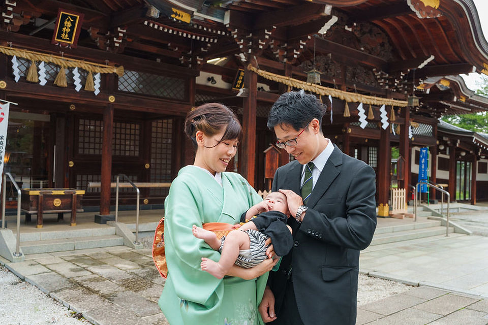 諏訪神社本殿前で赤ちゃんを抱っこする両親の笑顔の家族写真｜立川