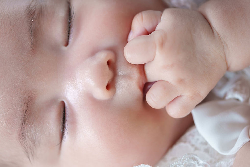 赤ちゃんが親指を口に当てながら眠っている、顔のクローズアップ写真。柔らかな肌と仕草が愛らしい。
