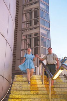 Bride in a Peter Pan-themed blue dress descending golden-lit steps with her partner during a Tokyo city photo session