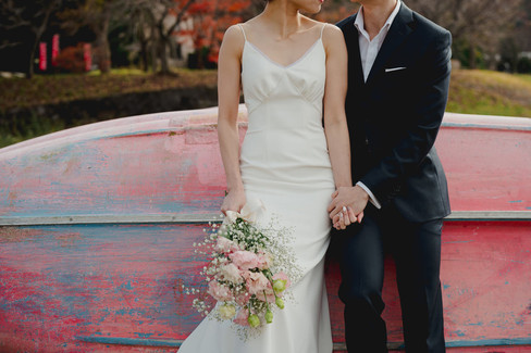 ピンクのボートを背景に、手をつないだ新郎新婦。ブーケの淡い色合いが印象的な1枚。
