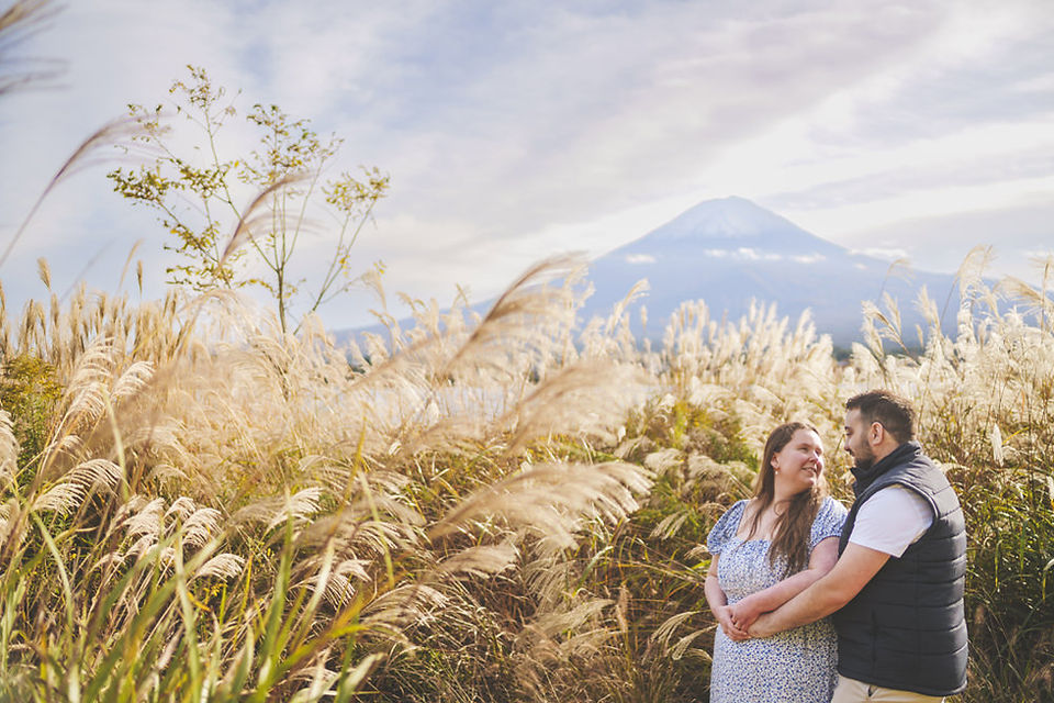 Romantic engagement portrait at Lake Kawaguchiko, couple surrounded by pampas grass with Mt. Fuji softly visible in the background