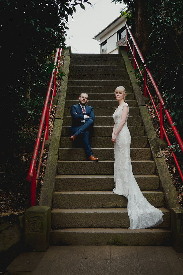 Bride and groom posing on stone stairs with red handrails, moody outdoor wedding portrait in Tokyo