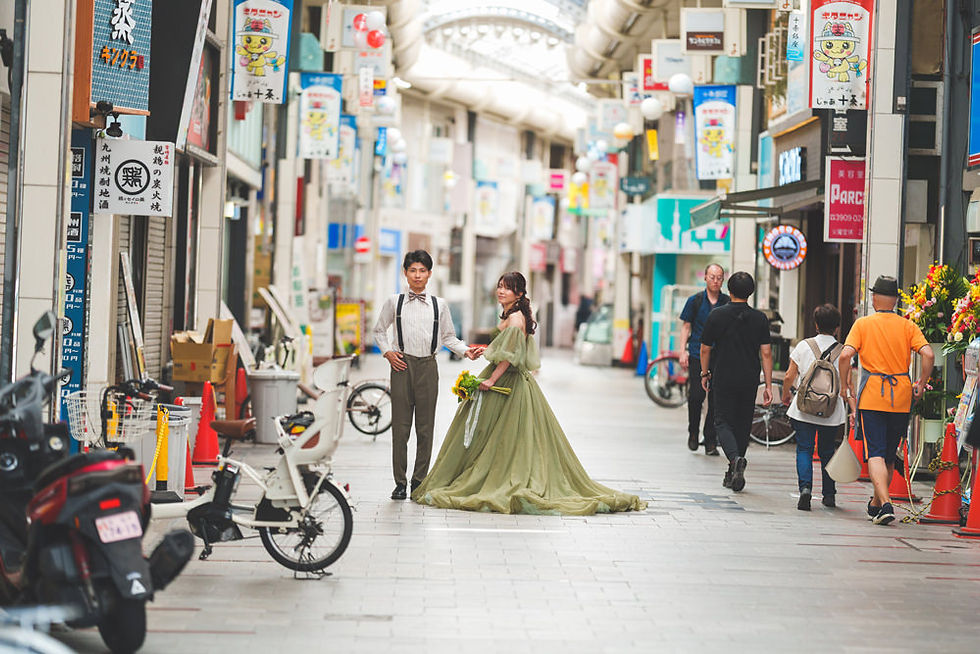 十条銀座商店街のアーケード内を手を取り歩く新郎新婦と、行き交う地元の人々が写る前撮り写真。