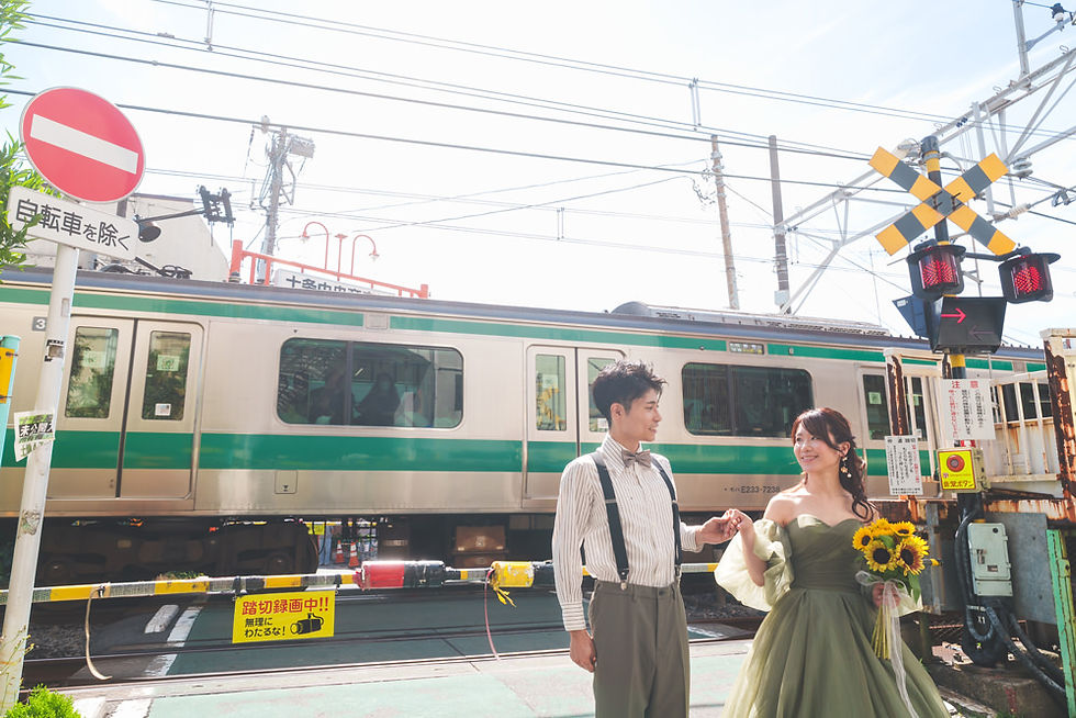 　埼京線の電車が通過する踏切を背景に、新郎が新婦の手を取って歩く十条でのフォトウェディング。