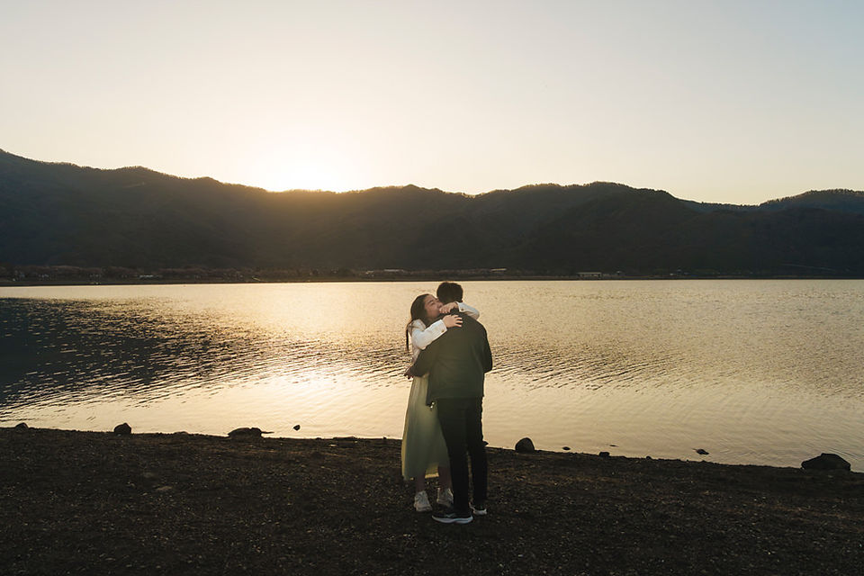Couple embracing by Lake Kawaguchiko after a sunrise proposal with golden morning light over the water