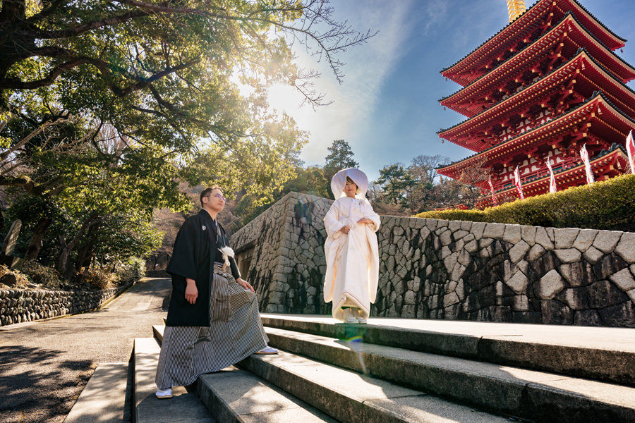 高幡不動尊の五重塔を背景に、階段をゆっくりと歩む和装の新郎新婦