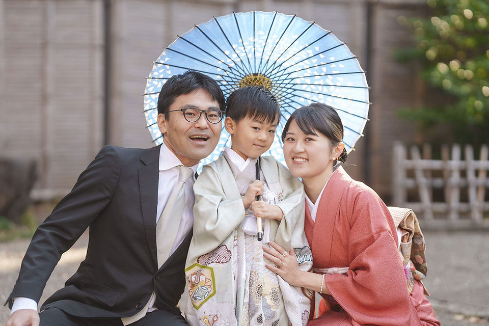 靖国神社で七五三撮影をする5歳男の子と両親 和傘を背景にした家族写真