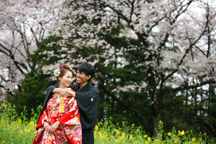 桜の木の下で見つめ合いながら寄り添う和装のカップル、春らしい柔らかな雰囲気