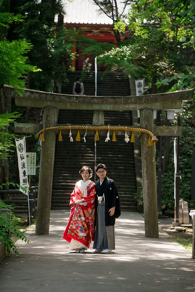 Couple in wedding kimono standing beneath a stone torii gate at Kita-in Temple in Kawagoe