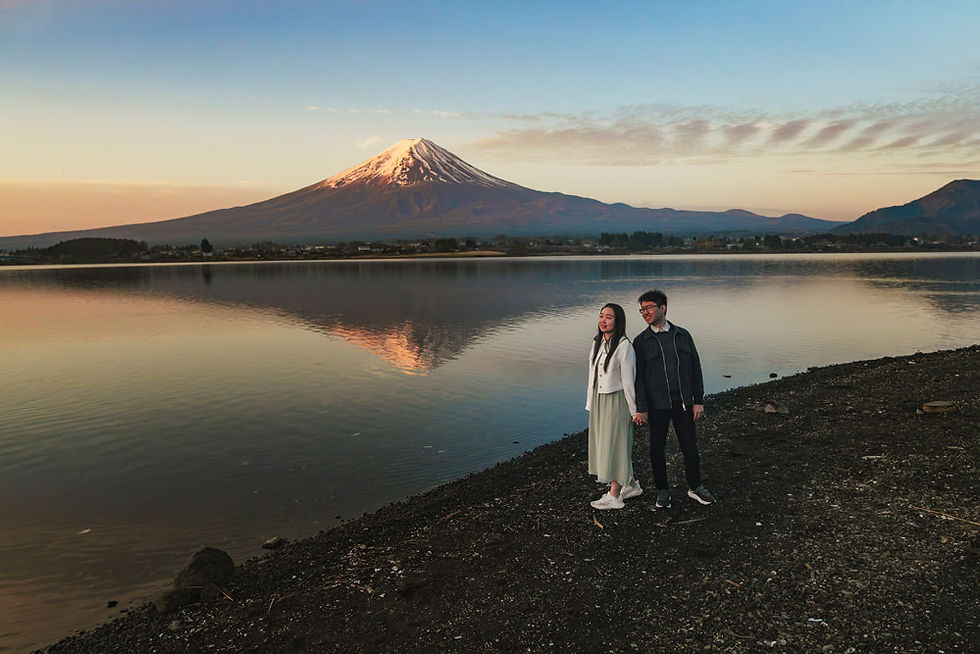 Couple holding hands beside Lake Kawaguchiko at sunrise with Mt. Fuji reflected in the calm water
