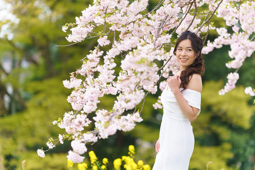 Bride in an off-shoulder wedding dress posing beneath blooming cherry blossoms during a spring pre-wedding photo session in Japan.