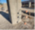 On a construction sight, three pieces of rebar that are protruding horizontally from a concrete pillar, whose ends are capped off with red caps to prevent anyone from walking into them and being impaled.