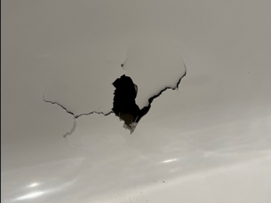 A large crack in a shower wall, showing a dark hole.. The surrounding area is smooth and glossy.
