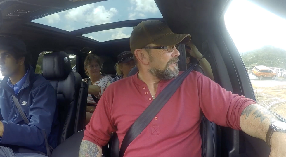 A man in a red shirt and baseball cap looks out of a 4X4 window.